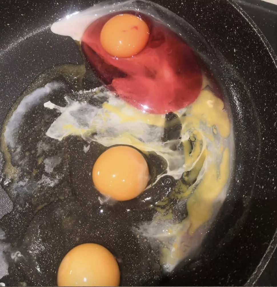 Pink egg alongside other normal eggs in a frying pan